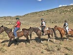 Three horseback riders smile as they ride past the camera.