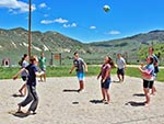 A group of youth keep their eyes on the ball in the sand volleyball court.