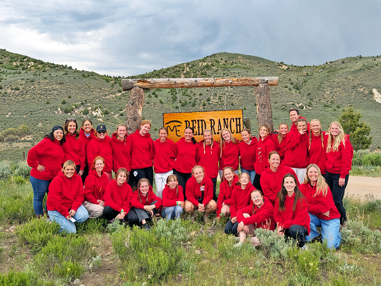 Young women in red sweaters pose in front of the Reid Ranch entry sign for their group photo.