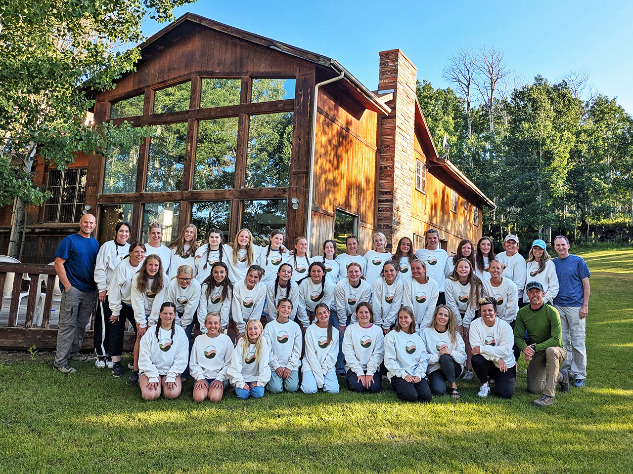 Young women dressed in matching sweaters pose in front of the Red Creek Lodge for their group photo.