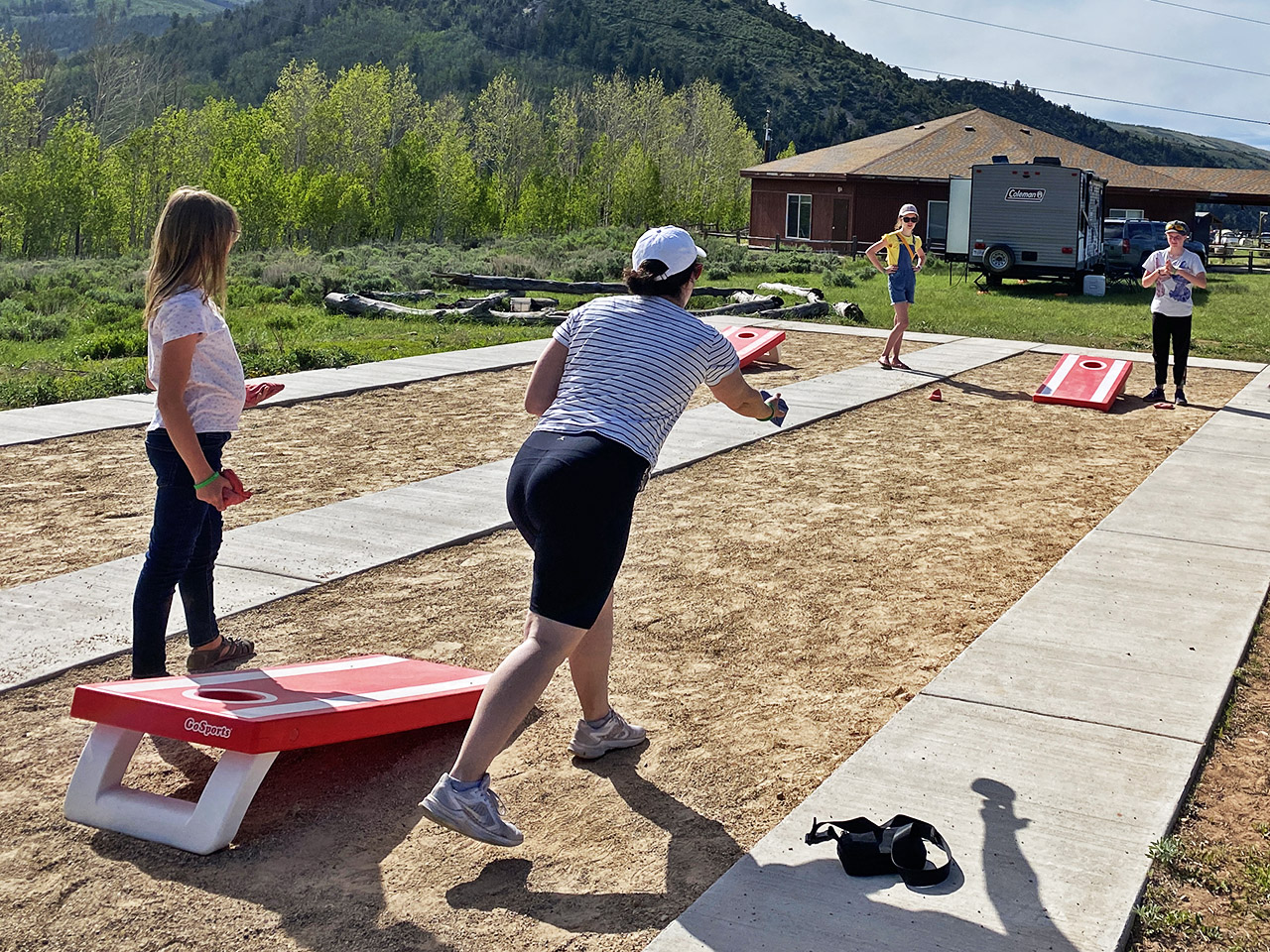 Two teams of two women play cornhole. Action shot of one lady tossing the bag.